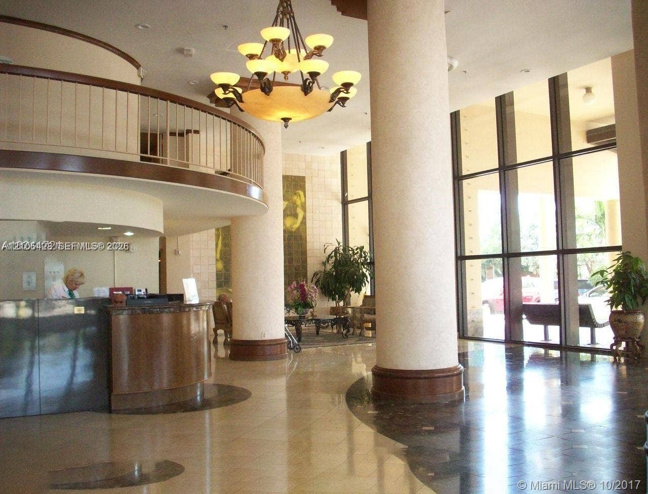 Two-story foyer featuring a grand chandelier, curved architectural balcony, tall window panels, and polished flooring with circular inlay