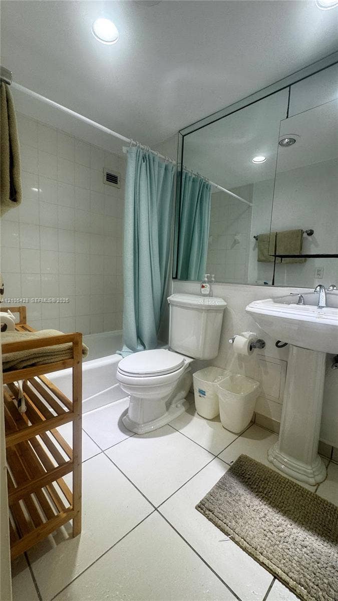 Pedestal sink, white tile flooring, recessed lighting, and a built-in tub with shower