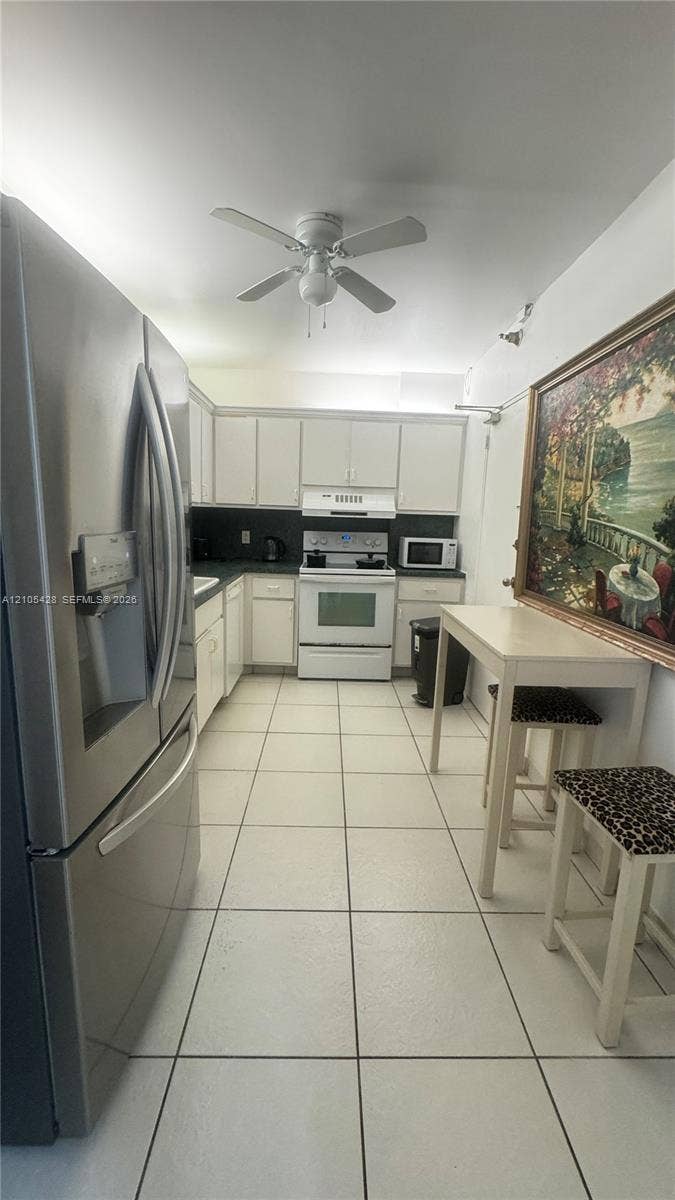 White tile flooring, white cabinetry, dark countertops, built-in range, and stainless steel refrigerator
