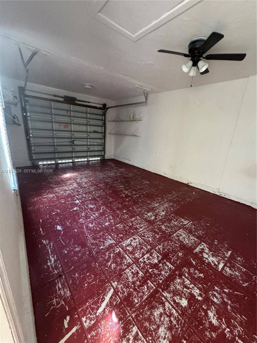 Garage space featuring a roll-up door, tiled flooring, built-in shelving, and a ceiling fan with integrated lighting