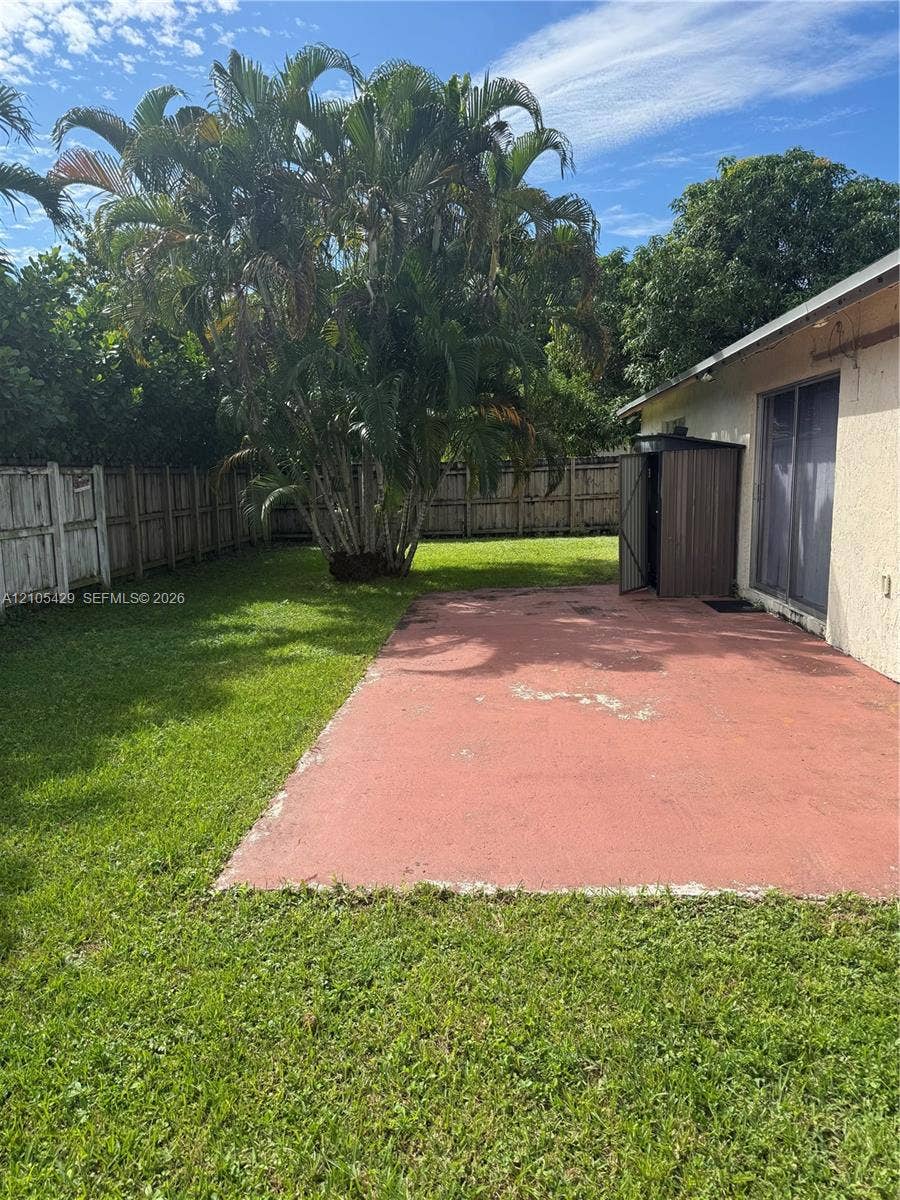 Expansive green lawn with a concrete patio, mature palm trees, and wood fencing