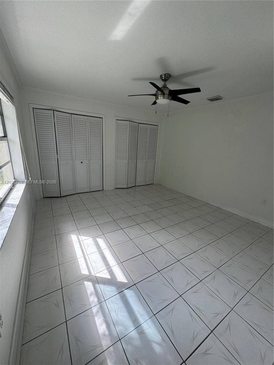 White tiled flooring, two sets of bi-fold louvered closet doors, and a ceiling fan with integrated lighting