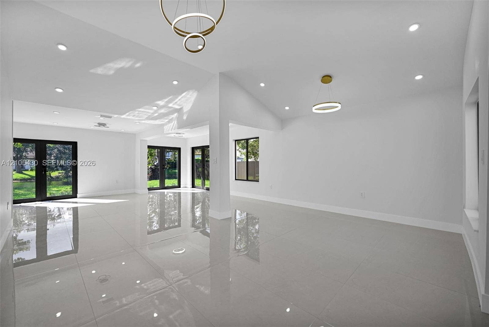 Large-format porcelain tile flooring, vaulted ceilings, recessed lighting, double-ring modern pendant fixtures, and black-framed French doors