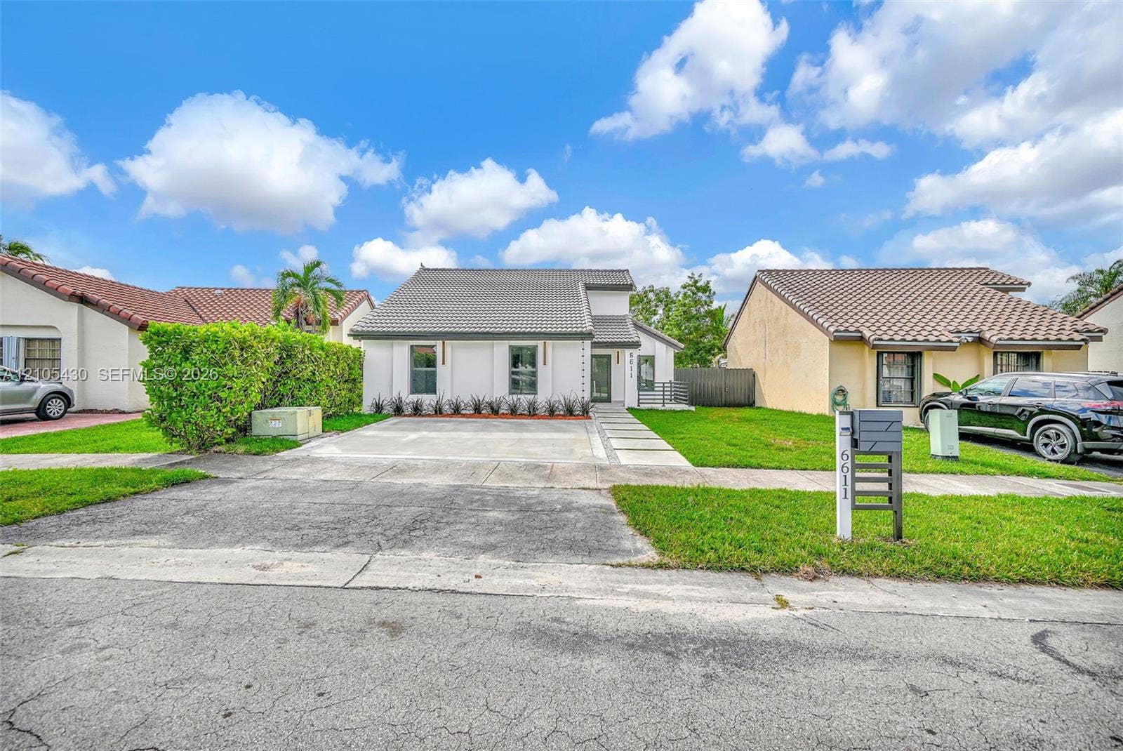 Single-story residence featuring a concrete tile roof, minimalist white stucco exterior, concrete paver walkway, and a landscaped front yard