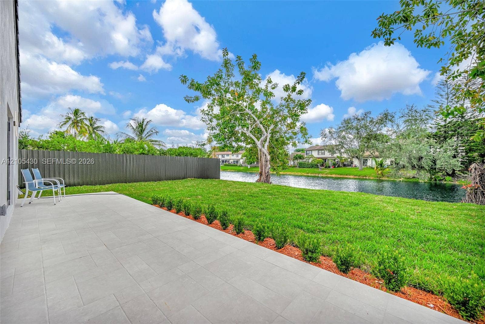 Backyard featuring a paved stone patio, manicured lawn, perimeter fencing, and waterfront exposure