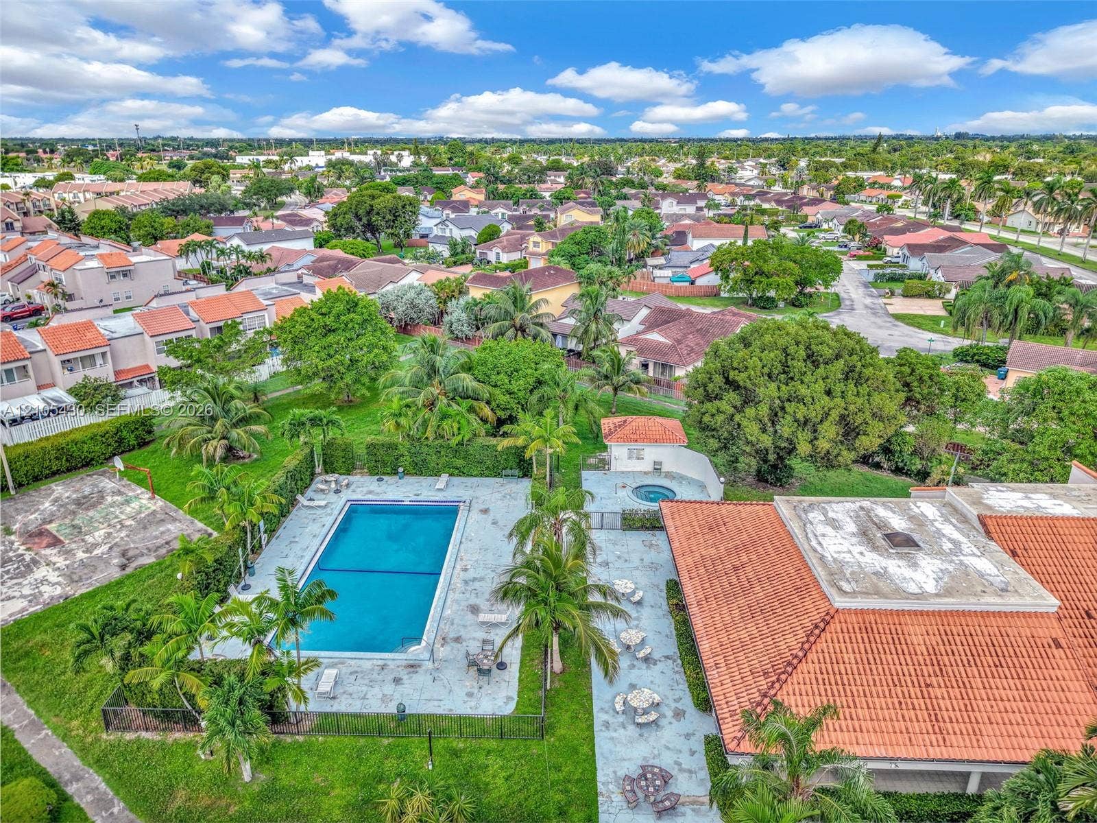 Outdoor recreational area featuring a rectangular swimming pool, separate spa, hardscaped patio, and tennis court, complemented by mature palm trees and landscaping