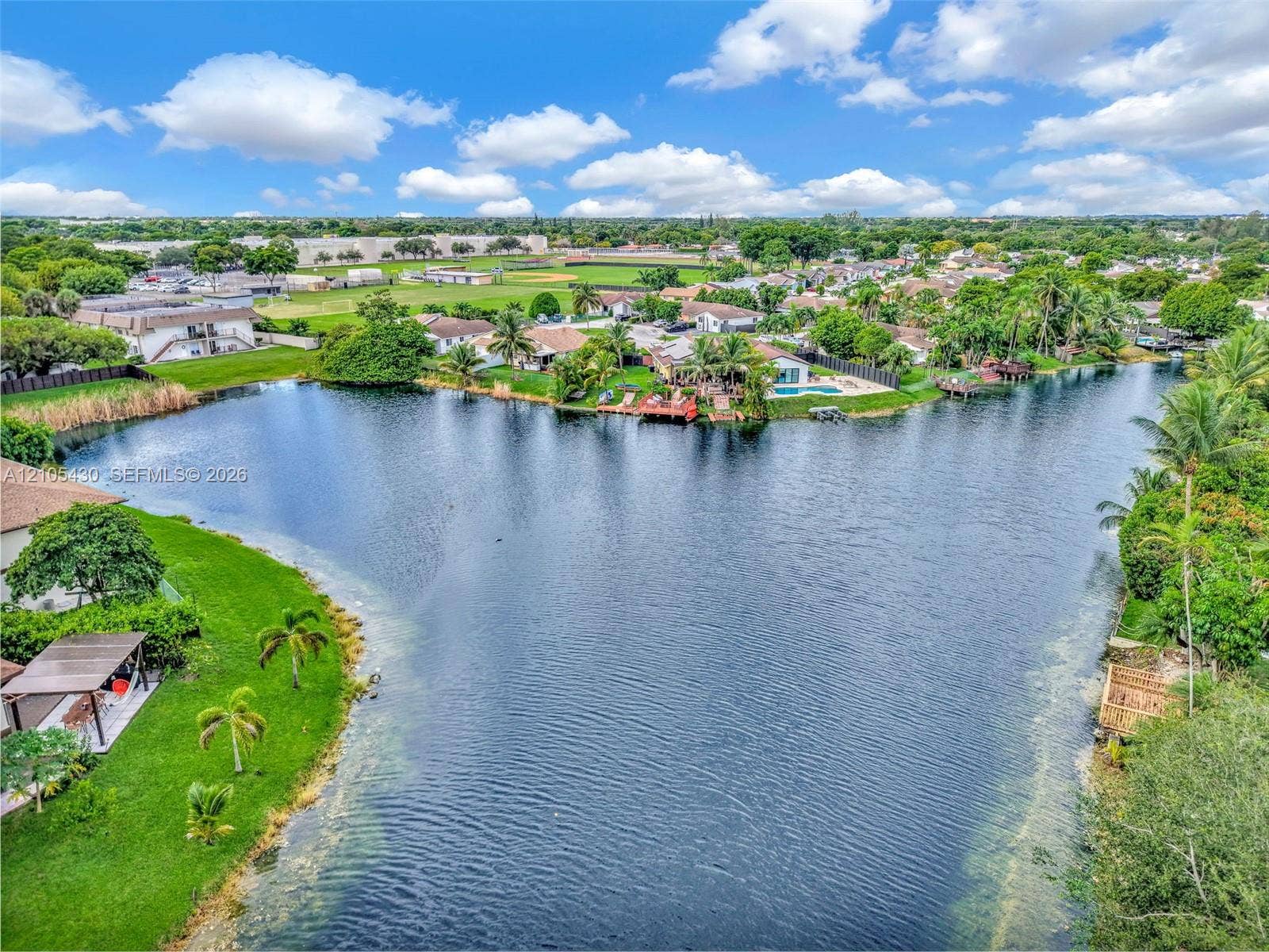 Waterfront property featuring a private shoreline, expansive lawn, mature palm trees, and a detached patio cover