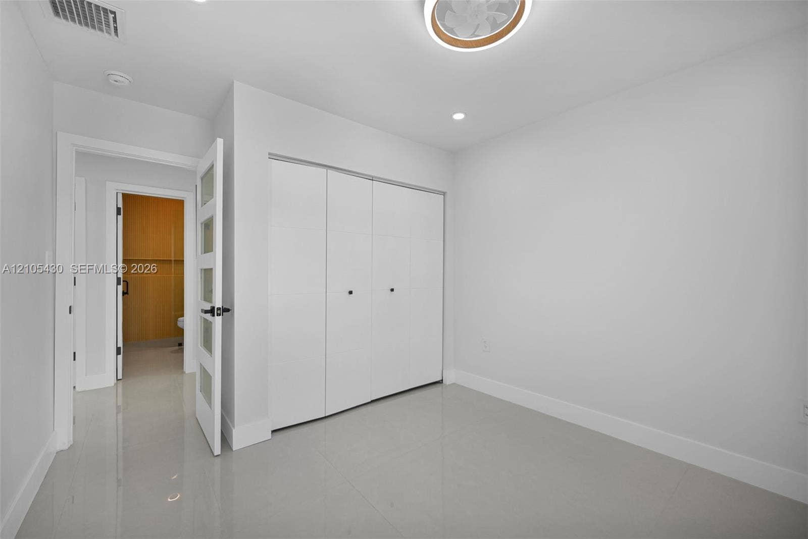 Neutral-toned interior space featuring light-colored tile flooring, a recessed ceiling fan, and a three-panel sliding closet