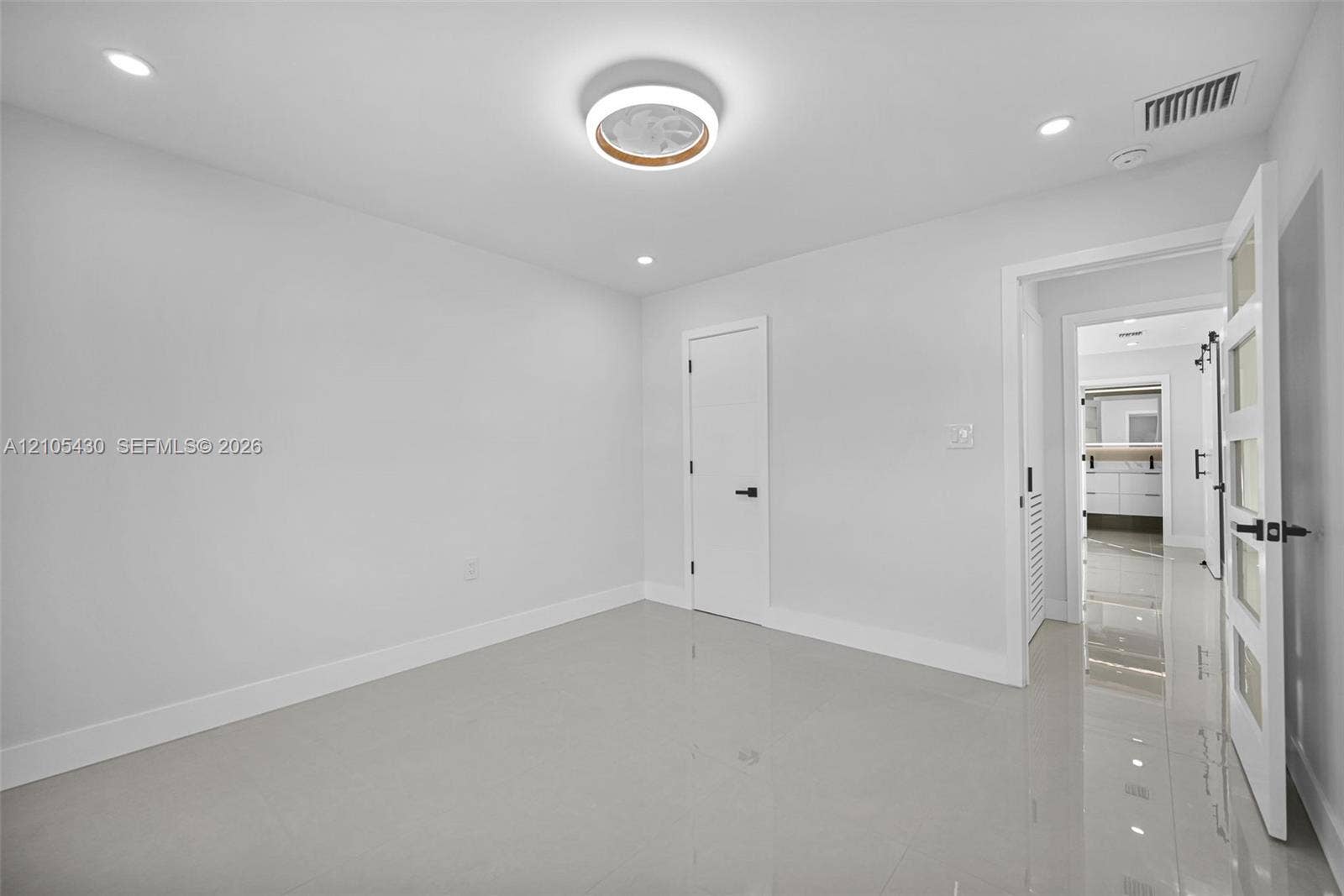 Interior room featuring polished tile flooring, recessed lighting, a modern circular flush-mount ceiling fixture, and a four-panel frosted glass door with matte black hardware
