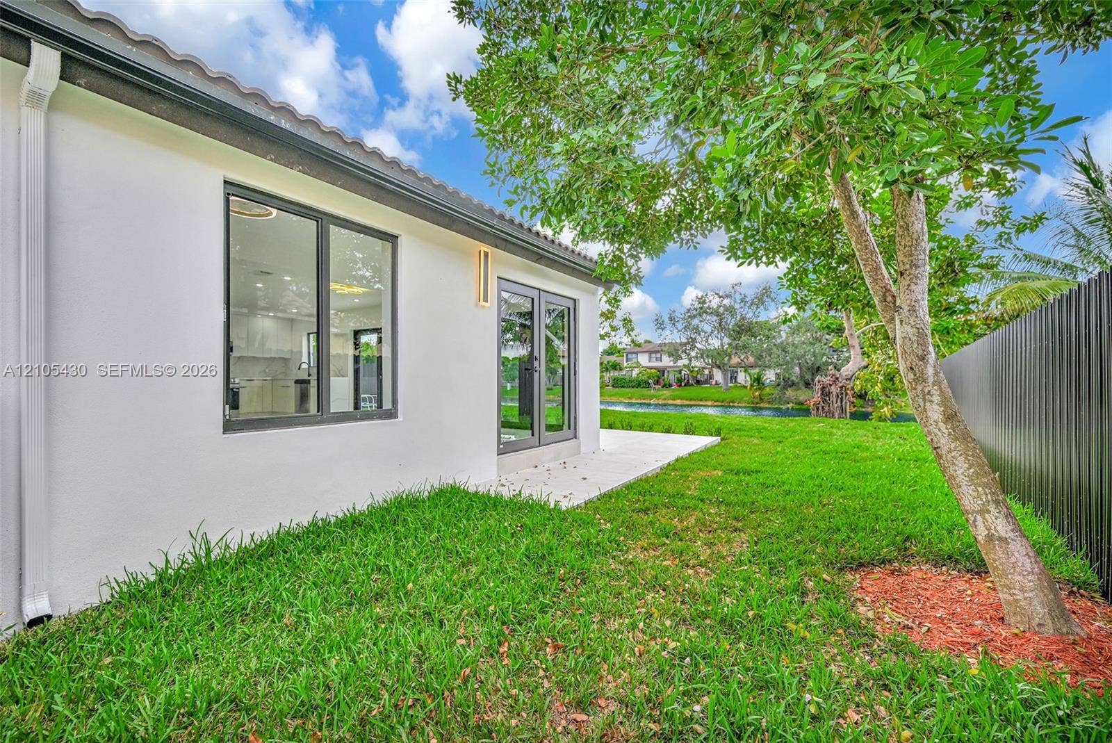 Exterior space featuring a concrete patio, white stucco siding, dark-framed dual glass doors, large windows, and a privacy fence