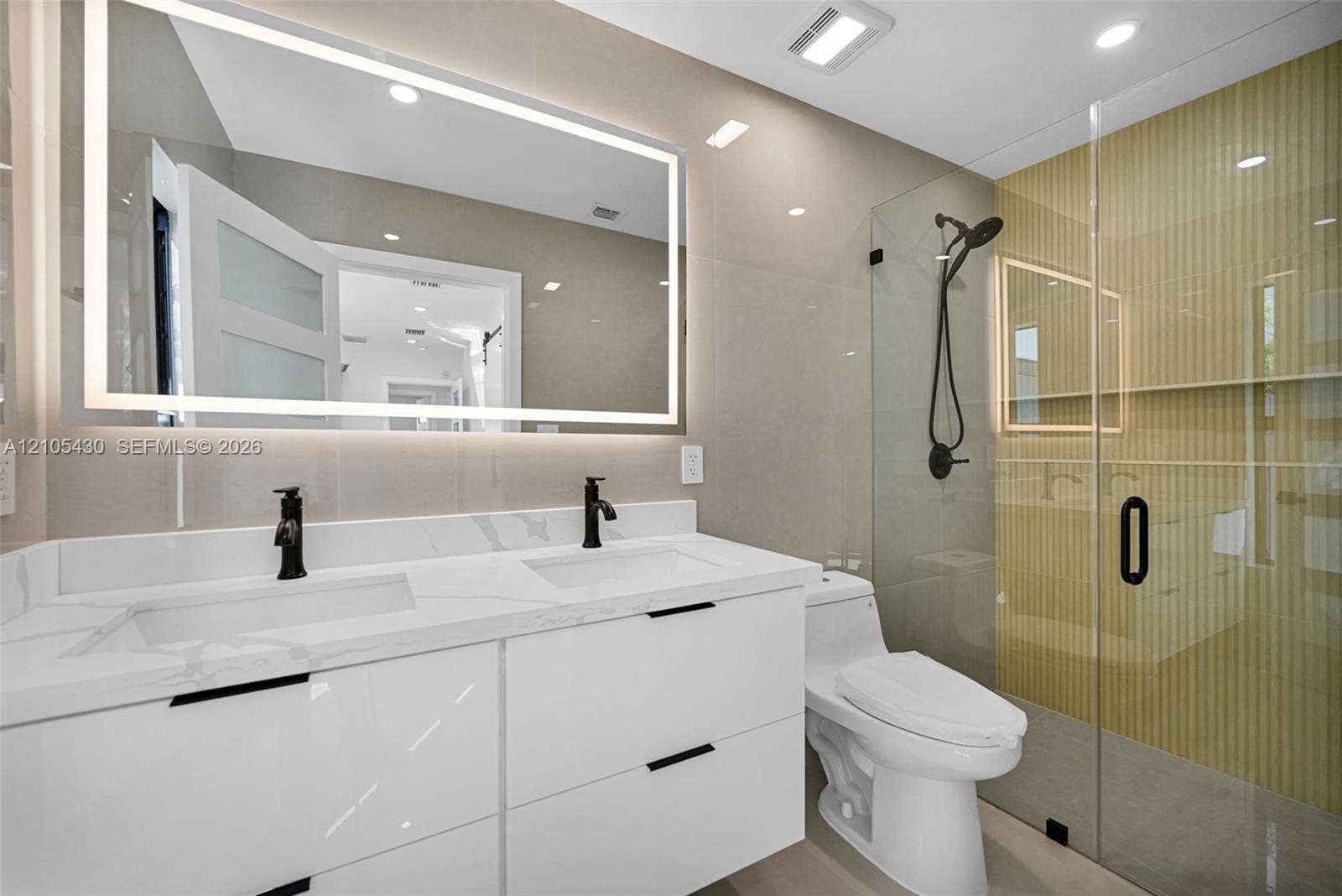 Dual-sink vanity with a solid-surface countertop, LED-backlit mirror, floor-to-ceiling tile, and walk-in shower with a glass enclosure and matte black fixtures