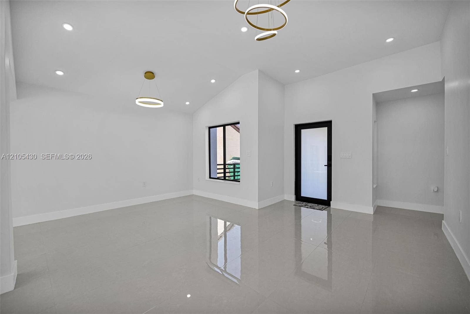 High-ceiling interior featuring glossy tile flooring, recessed lighting, modern geometric pendant fixtures, and a glass-paneled entry door with a matte black frame