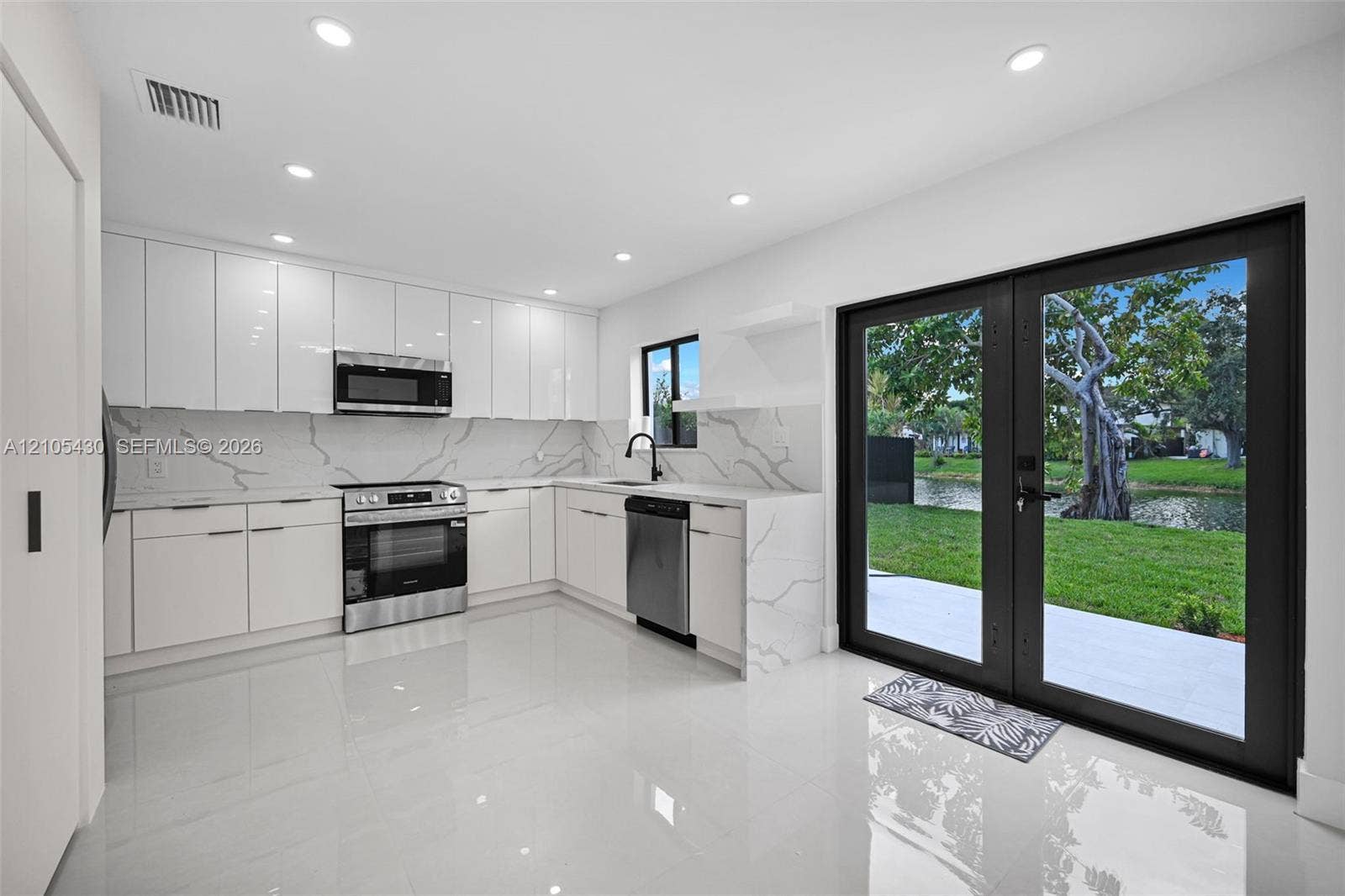 Kitchen featuring high-gloss white cabinetry, stone-finish backsplash with vein detailing, stainless steel appliances, polished tile flooring, and dual glass-paneled doors