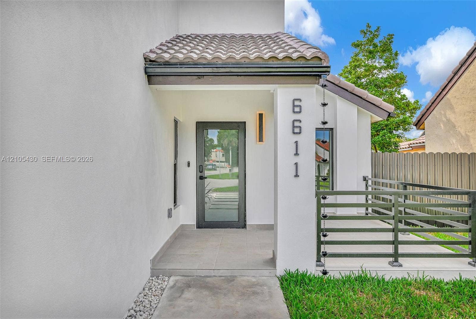 Covered entryway featuring a tiled porch, glass-panel door, metal chain downspout, and modern horizontal-slat railings