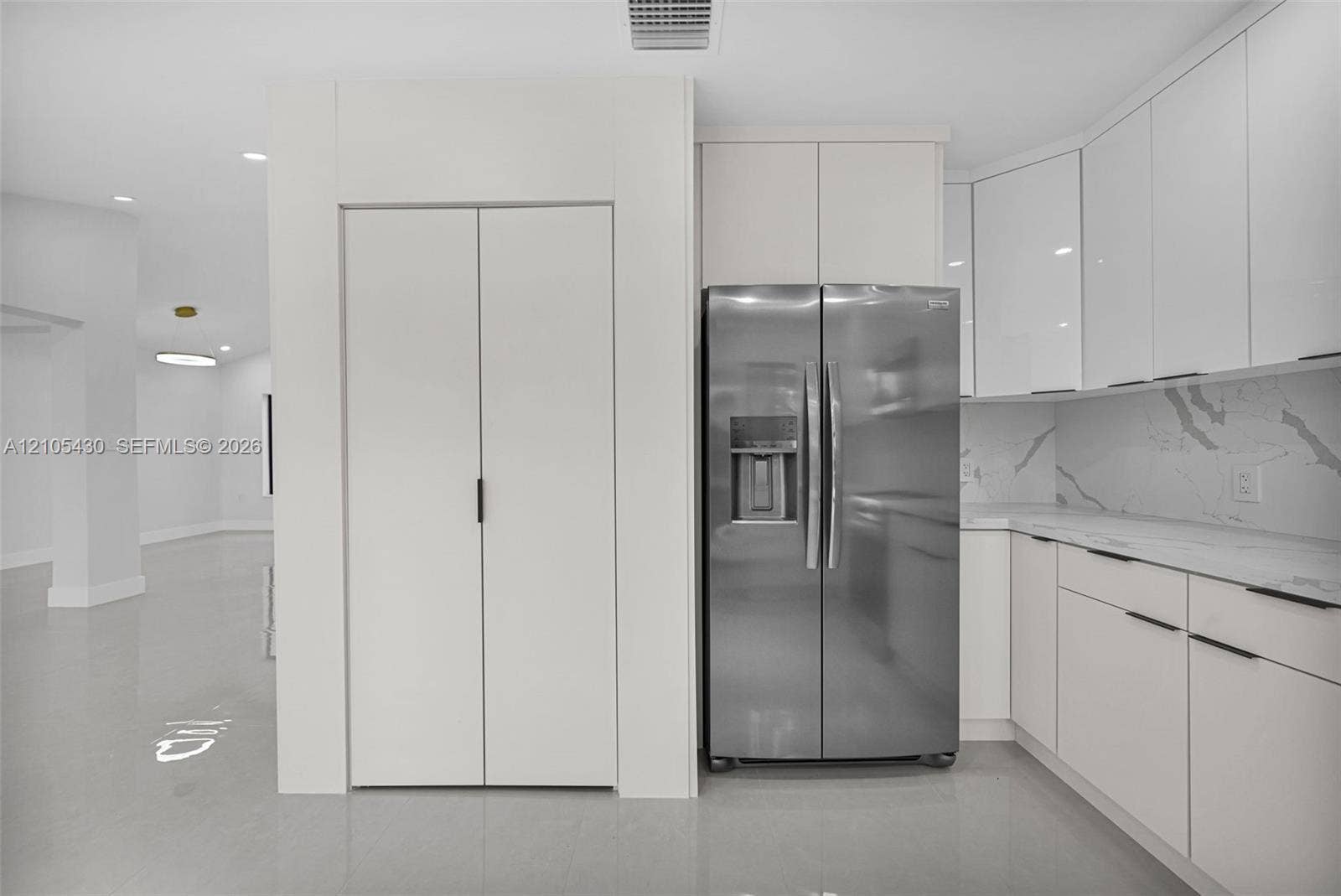 Kitchen featuring high-gloss white cabinetry, stone-patterned countertops, integrated stainless steel side-by-side refrigerator, and smooth-finish flooring