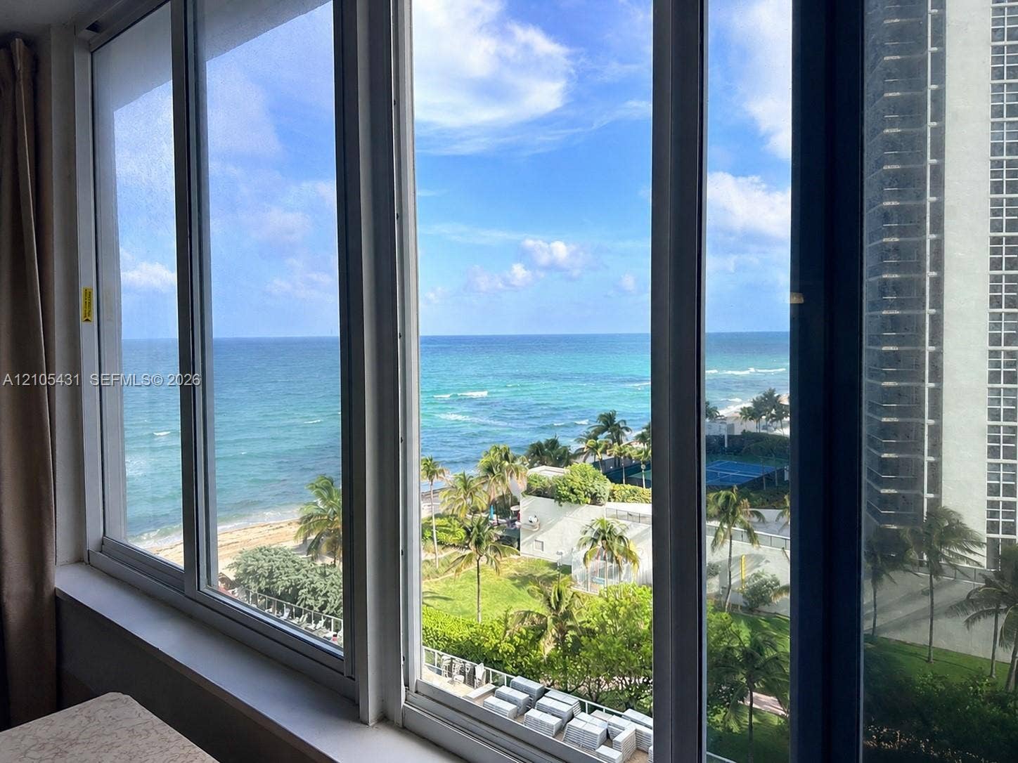 19201 Collins Avenue, #707, Sunny Isles Beach, FL 33160 Expansive ocean and beach scenery, framed by multiple large windows with white trim, overlooking a tropical landscape