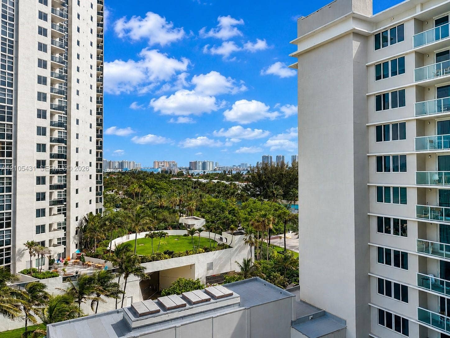 19201 Collins Avenue, #707, Sunny Isles Beach, FL 33160 High-rise building with multiple balconies, a rooftop amenity deck featuring a grassy area, surrounded by palm trees, and distant cityscape