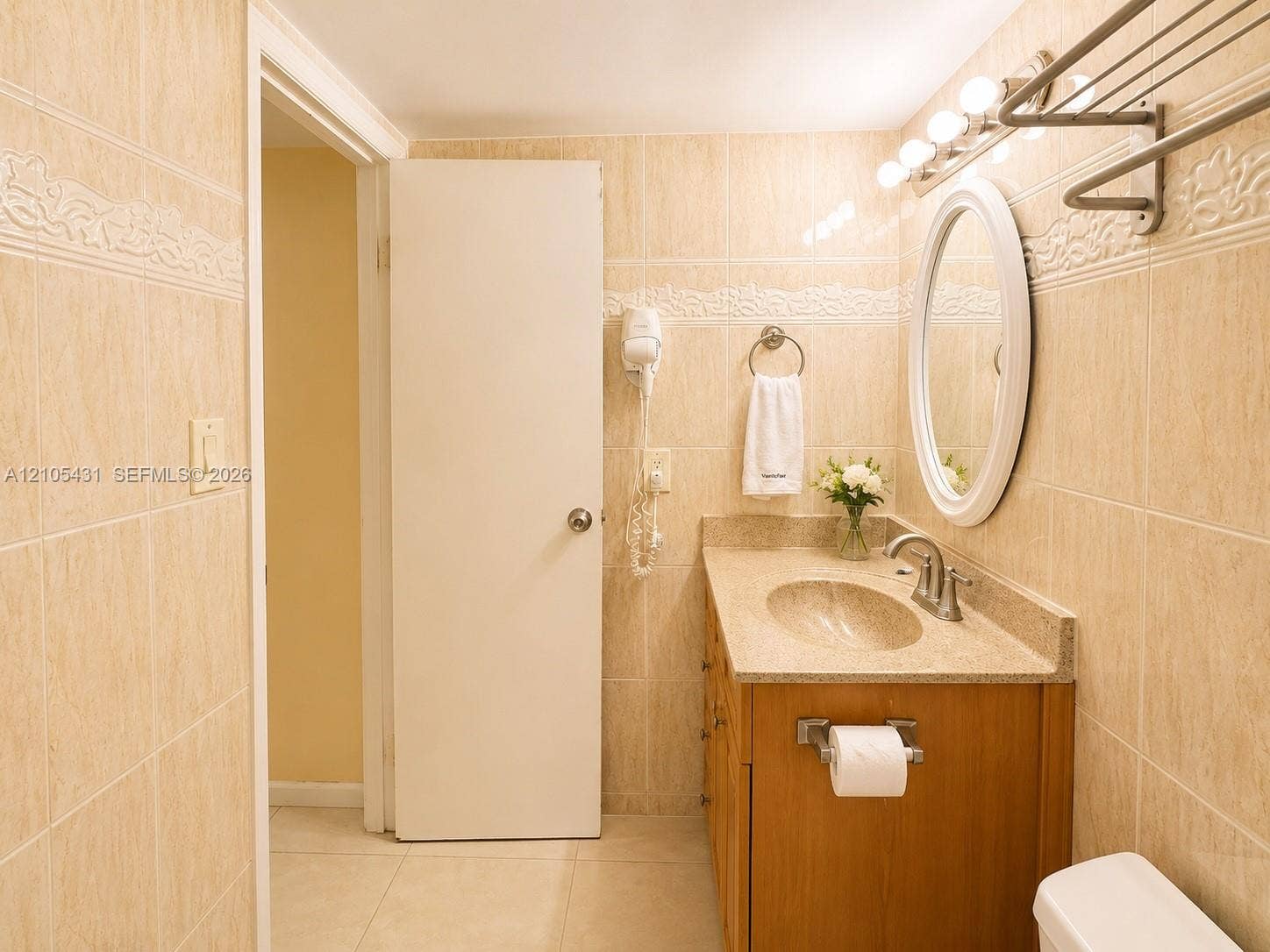 19201 Collins Avenue, #707, Sunny Isles Beach, FL 33160 Tiled bathroom featuring a wood-finish vanity with an integrated sink, an oval wall-mounted mirror, and a five-bulb vanity light fixture