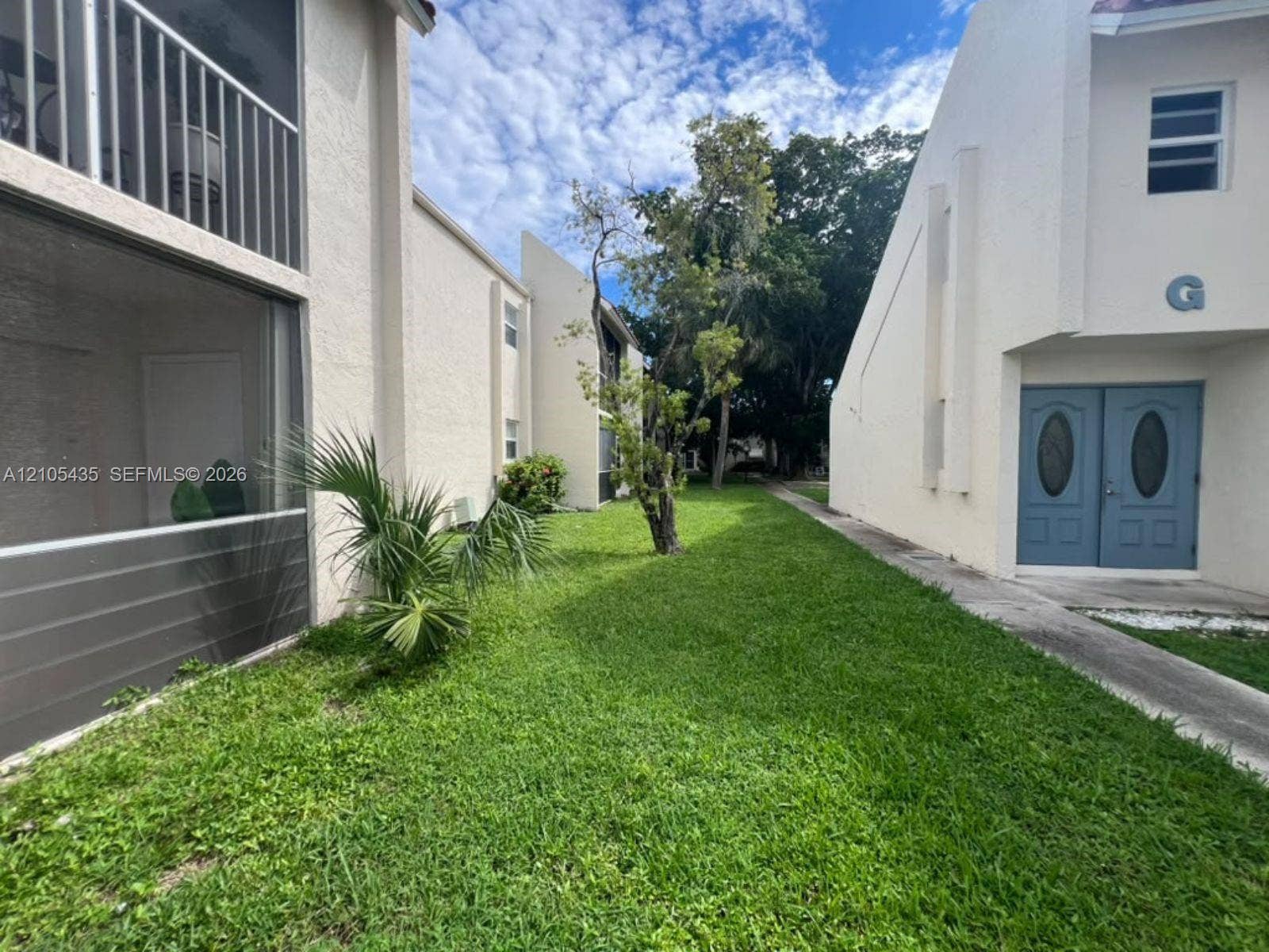 1428 SE 4th Avenue, #159, Deerfield Beach, FL 33441 Stucco exterior featuring dual-entry doors, a screened-in balcony, concrete walkways, and mature landscaping