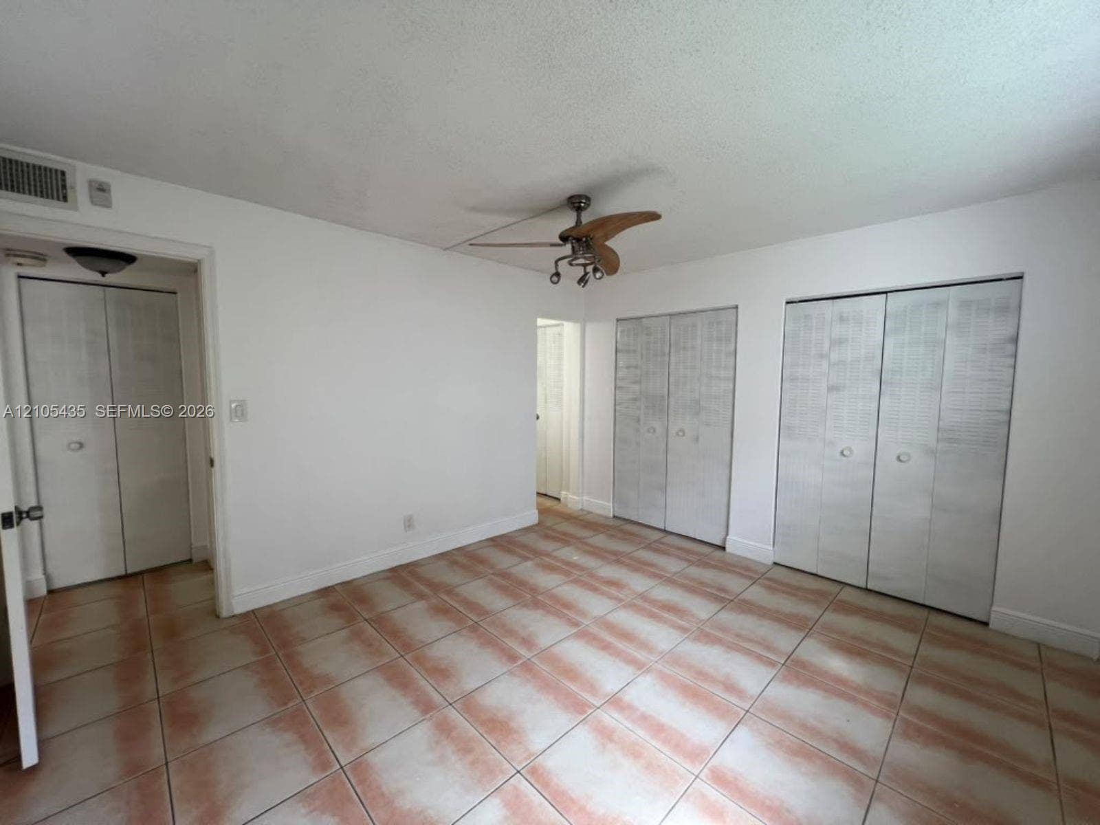 1428 SE 4th Avenue, #159, Deerfield Beach, FL 33441 Room featuring neutral-toned tile flooring, three sets of bi-fold closet doors, and a multi-blade ceiling fan with integrated lighting