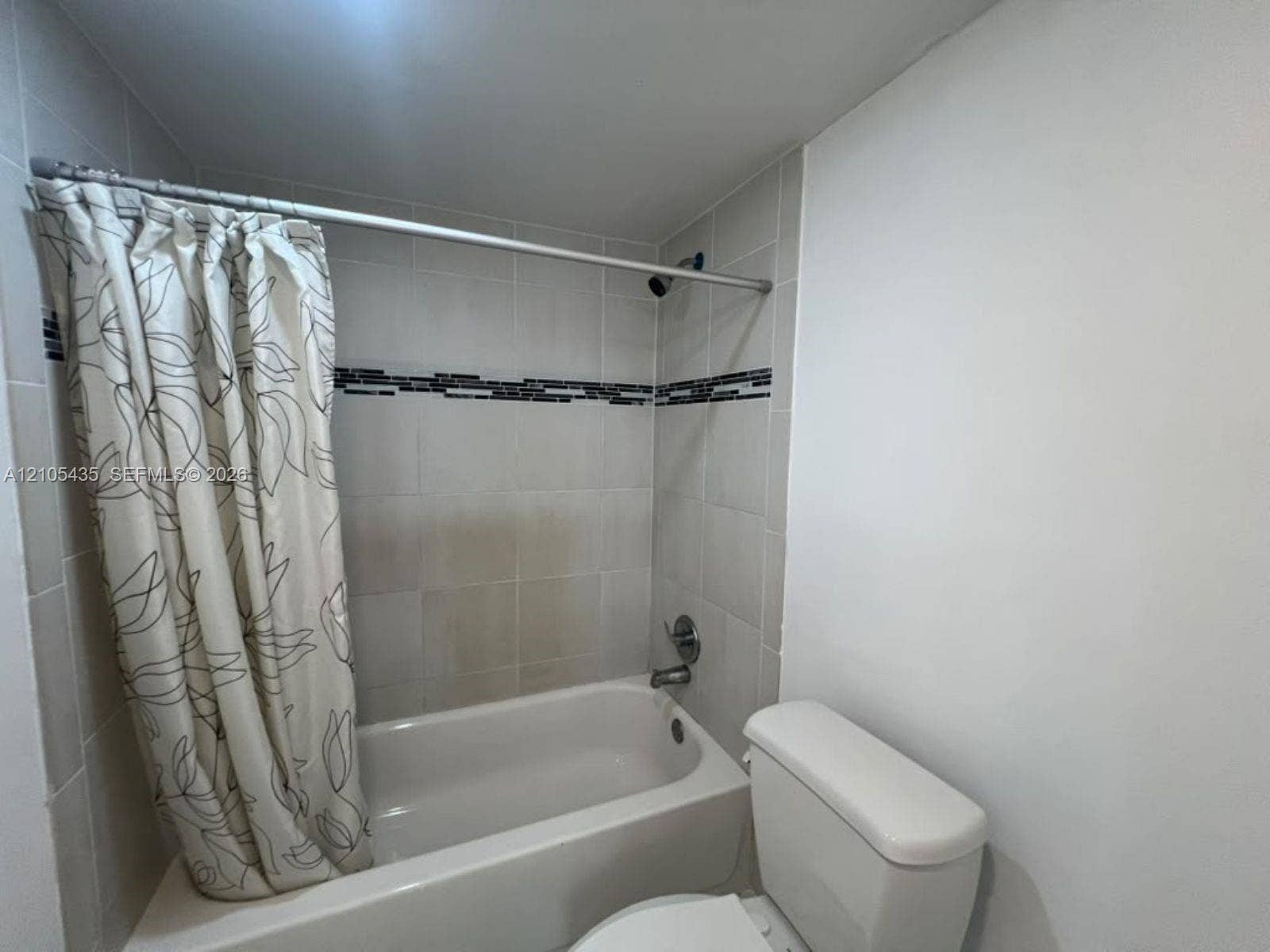 1428 SE 4th Avenue, #159, Deerfield Beach, FL 33441 Full-size bathtub with tiled surround featuring a decorative mosaic inlay, integrated shower fixture, and standard toilet
