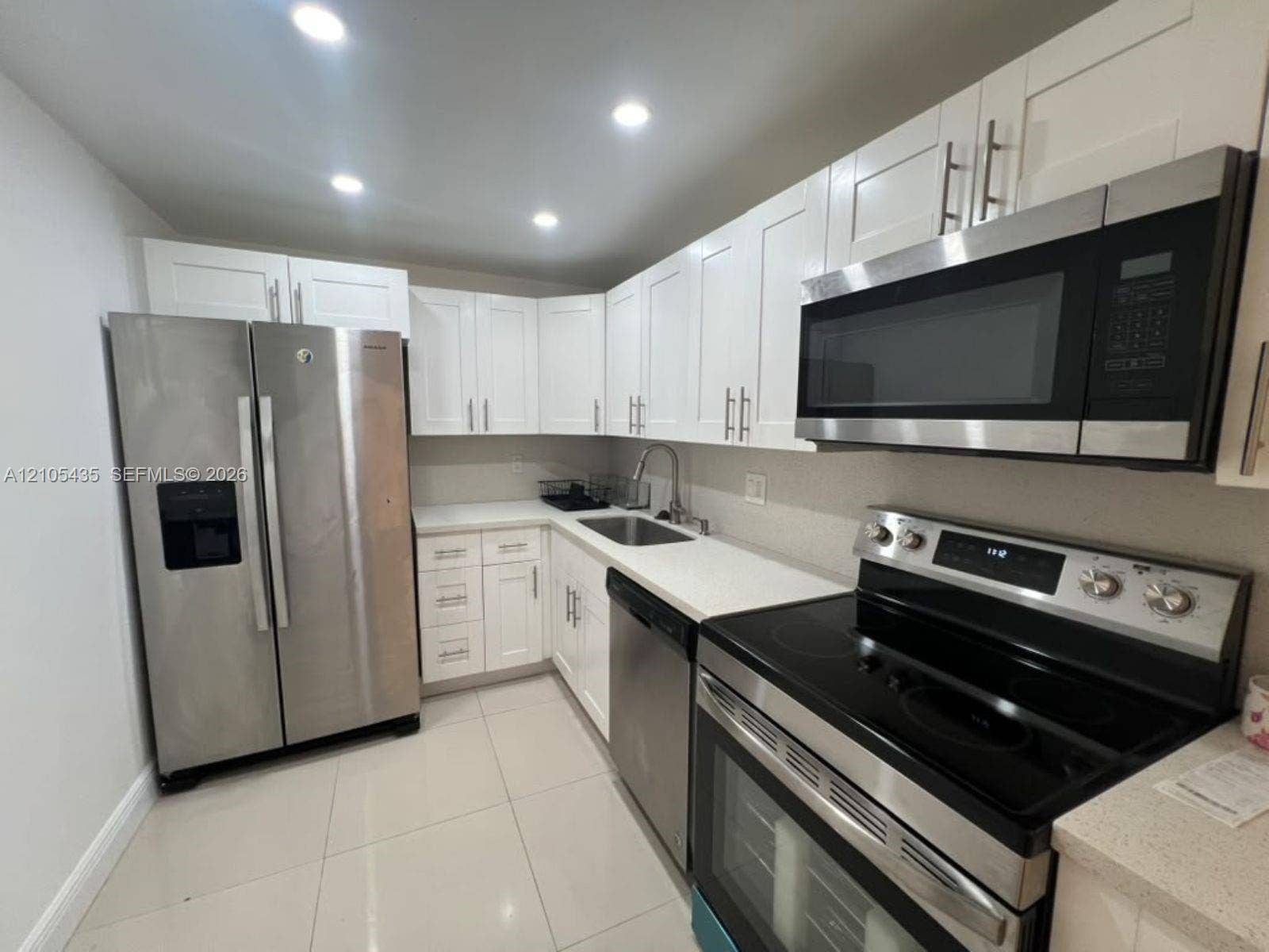 1428 SE 4th Avenue, #159, Deerfield Beach, FL 33441 Kitchen featuring white shaker-style cabinetry, stainless steel appliances, solid surface countertops, a stainless steel undermount sink, and large-format tile flooring