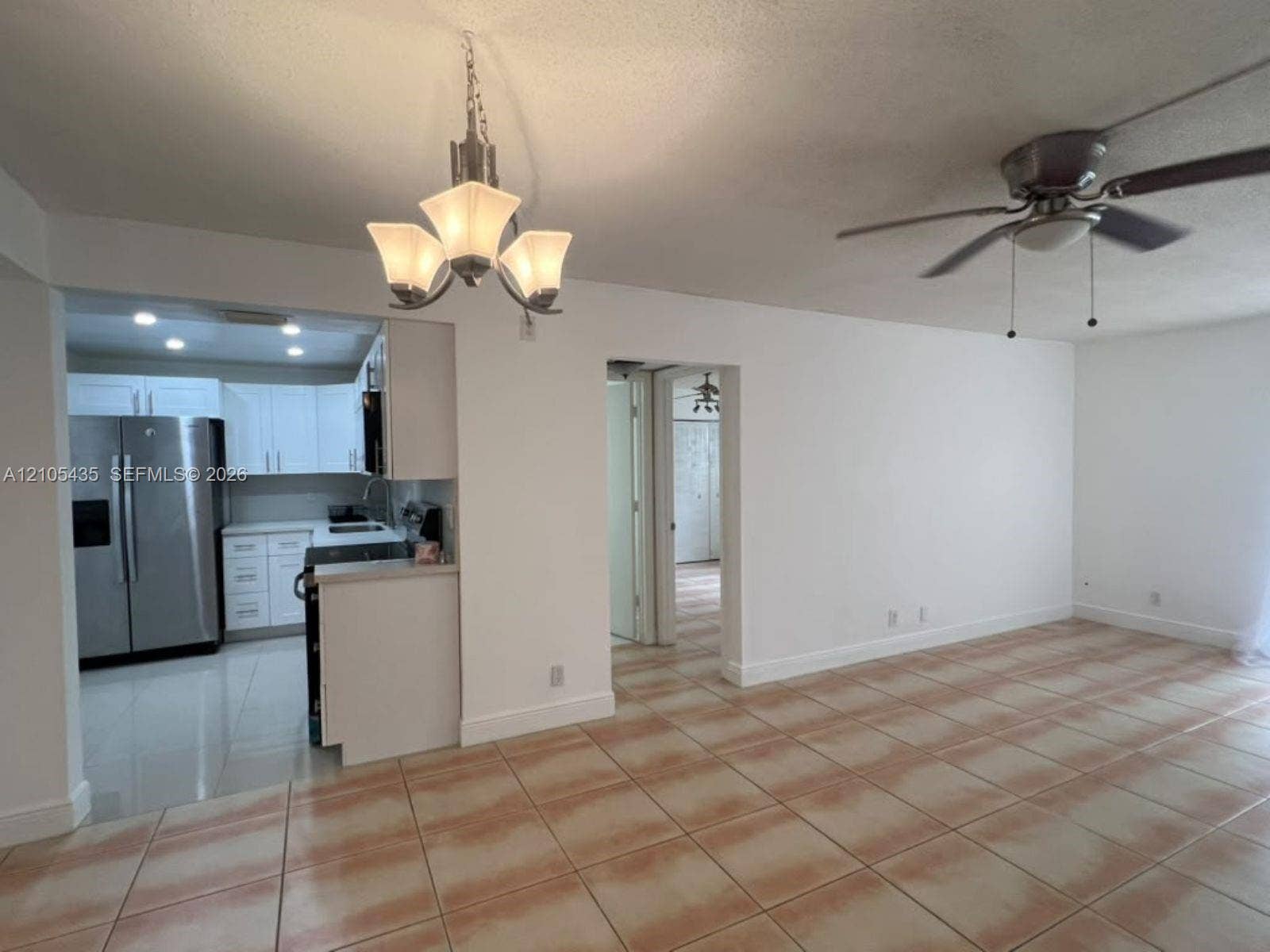 1428 SE 4th Avenue, #159, Deerfield Beach, FL 33441 Open-concept interior featuring light-toned tile flooring, white cabinetry, a brushed metal three-light chandelier, and a ceiling fan with integrated lighting
