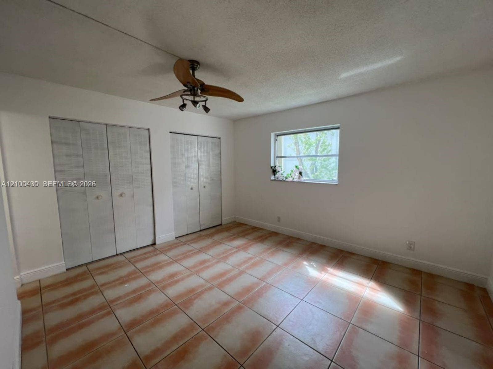 1428 SE 4th Avenue, #159, Deerfield Beach, FL 33441 Room interior featuring ceramic tile flooring, dual closet sets with bi-fold doors, and a ceiling fan with integrated lighting