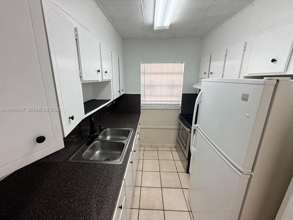 Galley kitchen featuring white cabinetry, dark speckled countertops, a double basin stainless steel sink, and tile flooring
