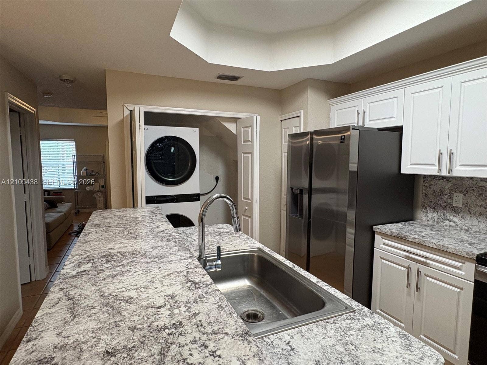 Kitchen featuring a stainless steel sink with a high-arc faucet, light-toned countertops, white cabinetry with silver-toned hardware, and a stainless steel refrigerator