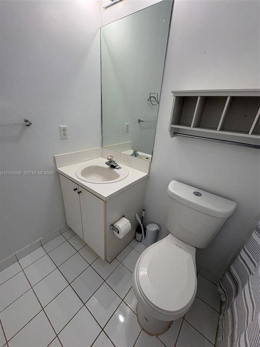 White tile flooring, wall-mounted rectangular mirror, vanity with integrated sink, and white toilet