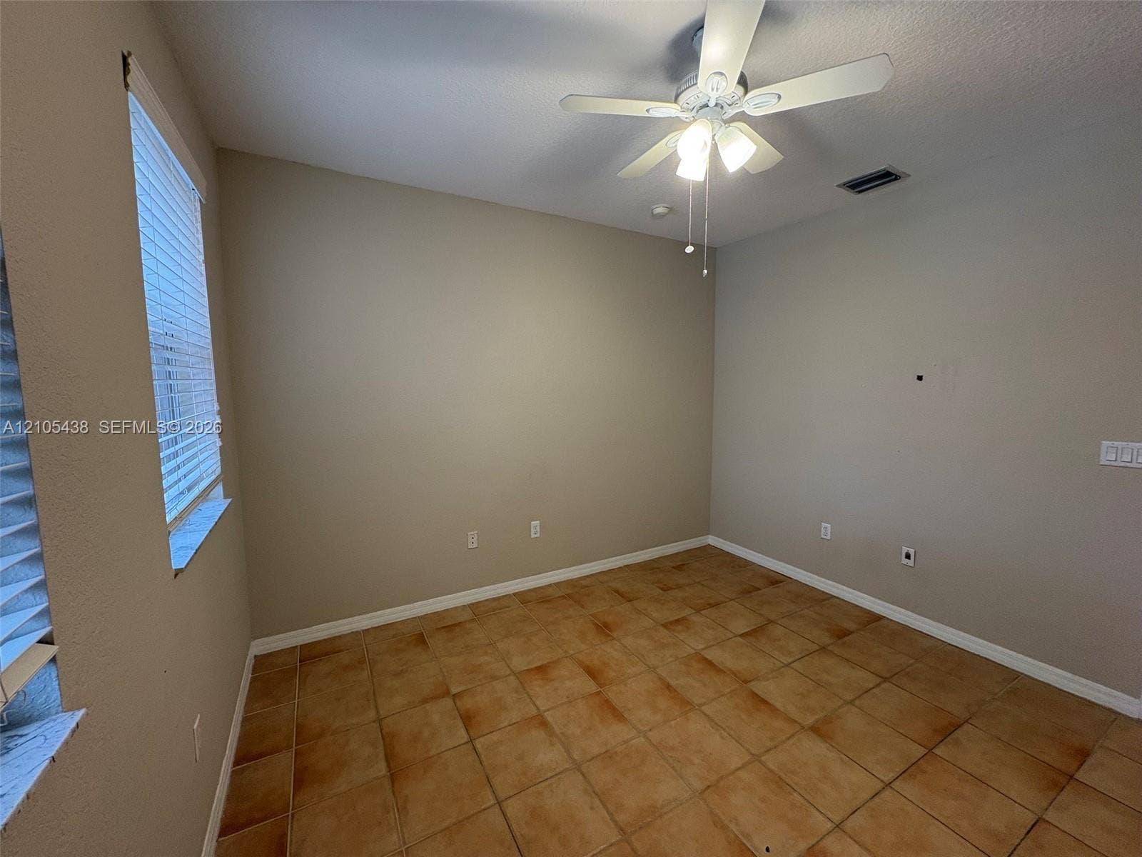 Warm-toned tile flooring, neutral wall tones, window with horizontal blinds, and a ceiling fan with integrated lighting