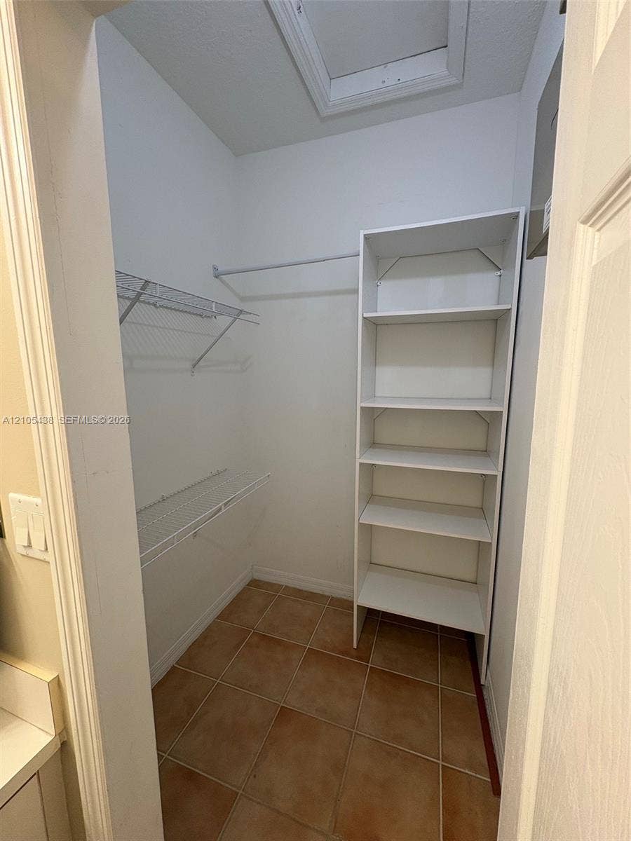 Walk-in closet with terra cotta tile flooring, white wire shelving, white storage shelving, and white walls