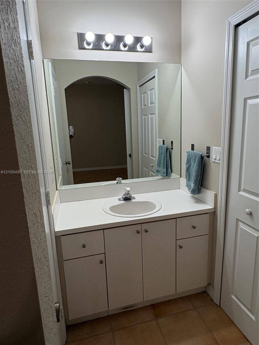 Vanity with an integrated sink, white countertop, white cabinetry with silver-tone hardware, and a large wall-mounted mirror