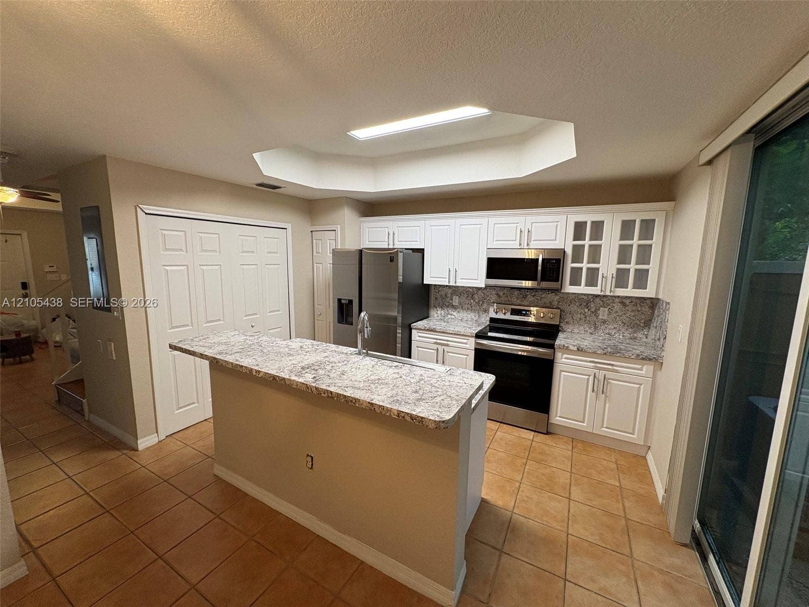 Kitchen featuring tile flooring, white cabinetry, a central island with a sink, stainless steel appliances, and a tray ceiling