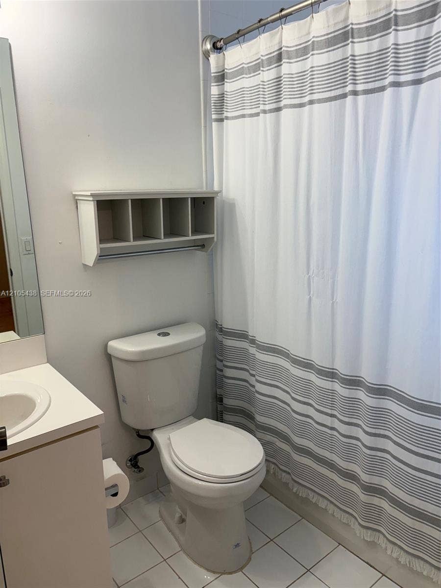 White tile flooring, white vanity with integrated sink, wall-mounted shelving, and a shower rod