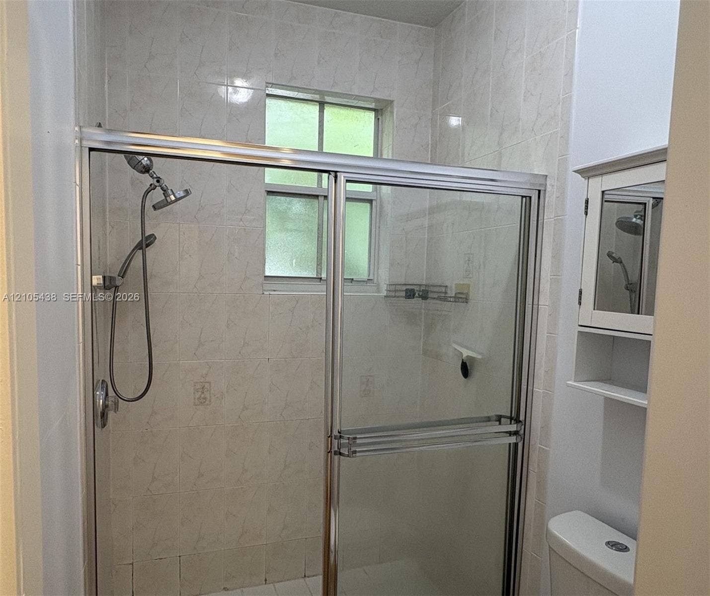 Tiled shower enclosure with a sliding glass door and an adjustable shower head