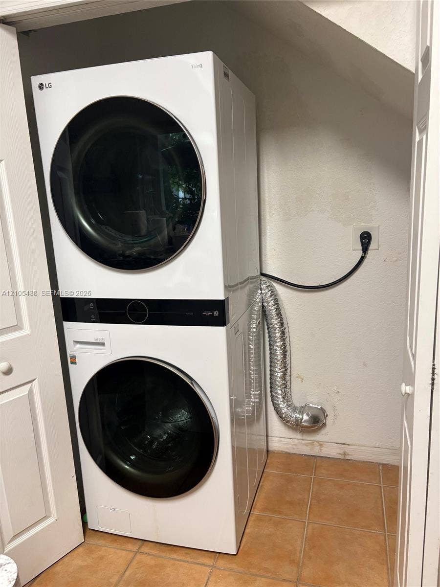 Stacked laundry appliances within a utility closet featuring tile flooring