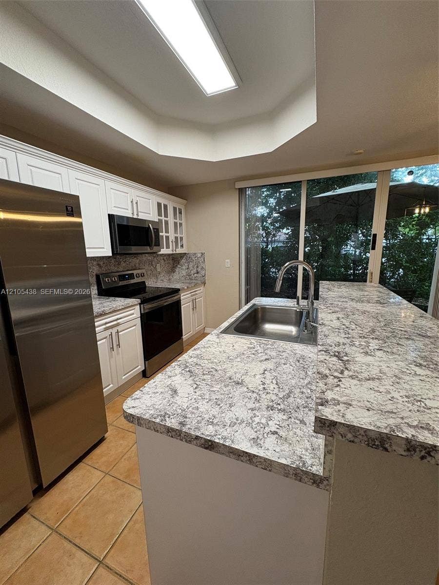 Kitchen with white cabinetry, stainless steel appliances, speckled countertops, and tile flooring