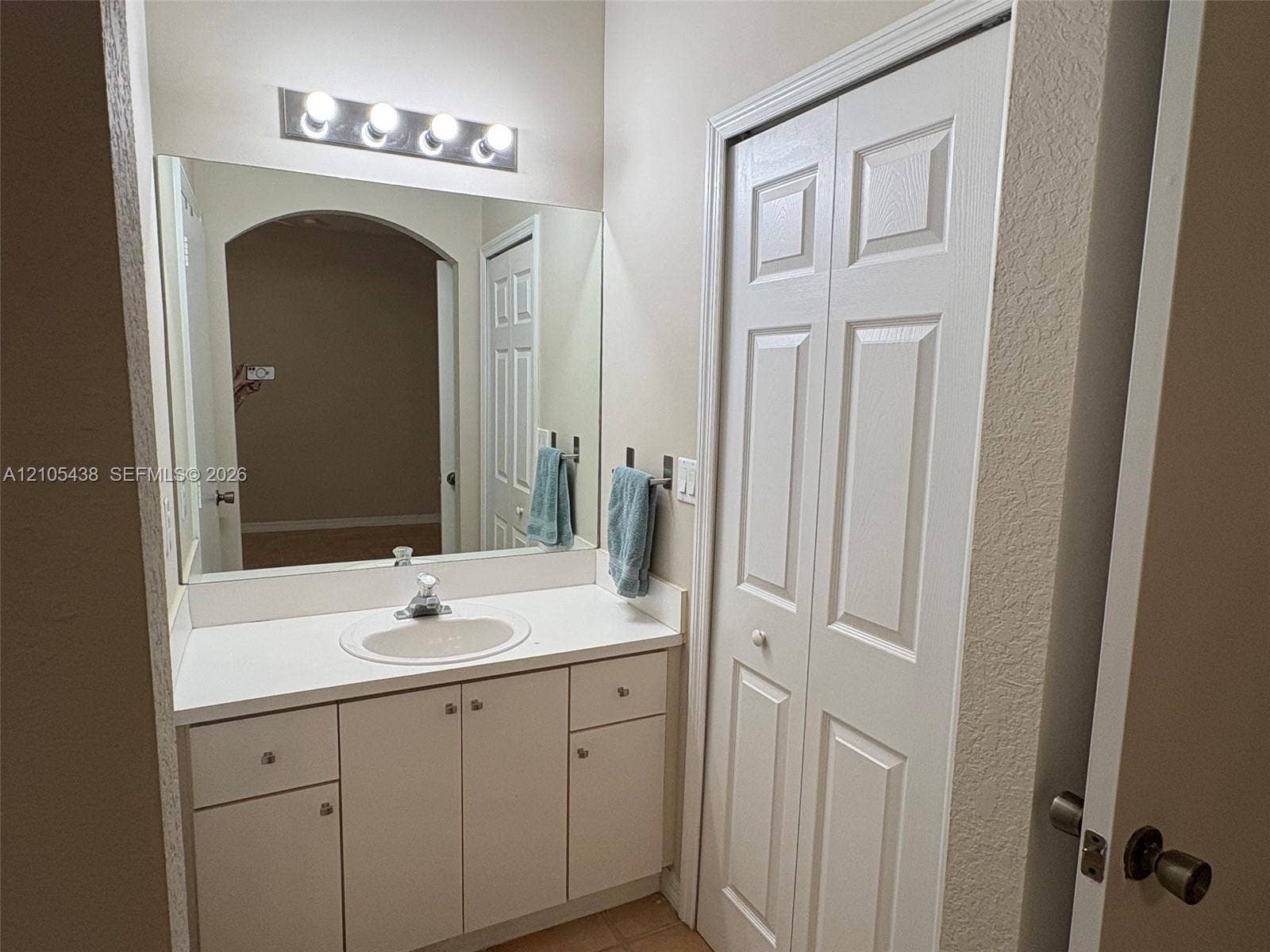 White vanity with an integrated sink and base cabinetry, complemented by a large wall mirror and a four-bulb light fixture
