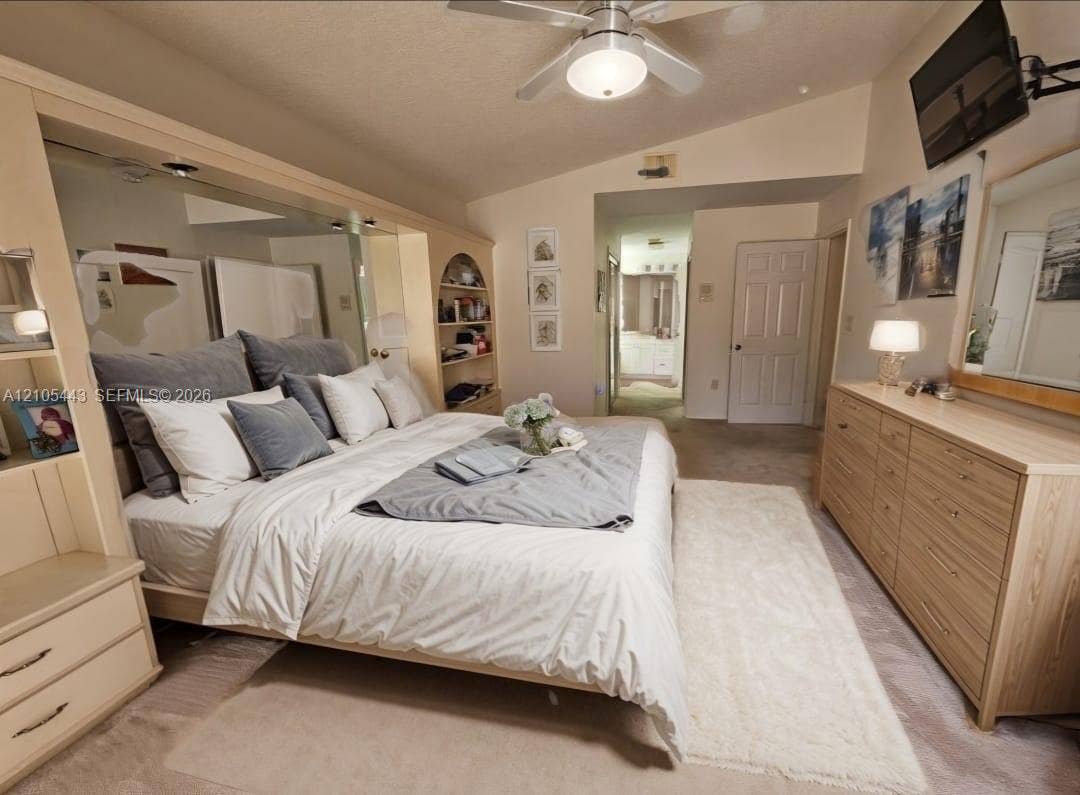 Vaulted ceiling, ceiling fan, carpet flooring, built-in shelving, and mirrored wall accents