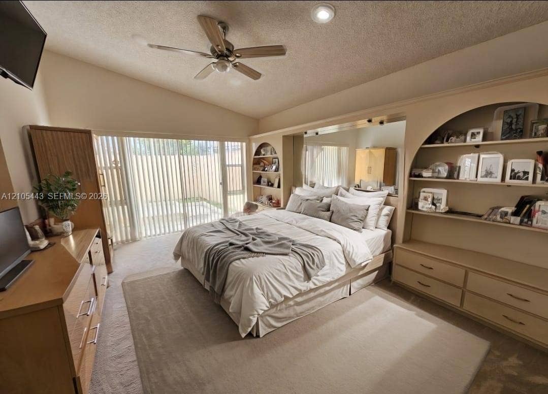 Vaulted ceiling, ceiling fan, recessed lighting, built-in shelving, and sliding glass door