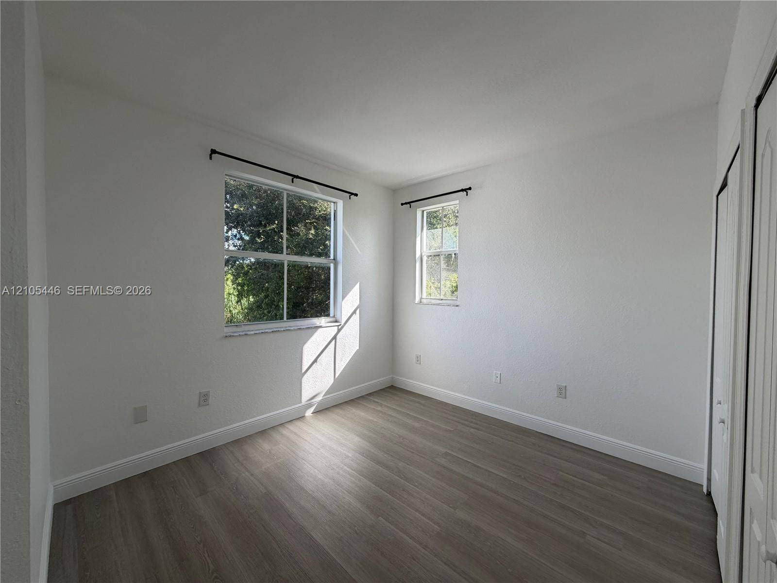 Wood-finish flooring, white painted walls, and window treatments with dark rods