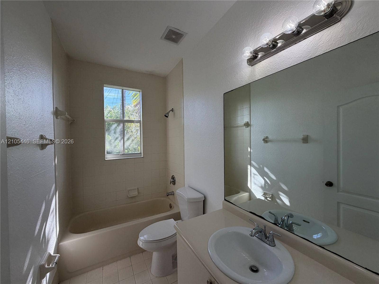 Bathroom featuring a vanity with an integrated sink, a large wall-mounted mirror, a four-bulb vanity light fixture, a toilet, and a bathtub with a shower