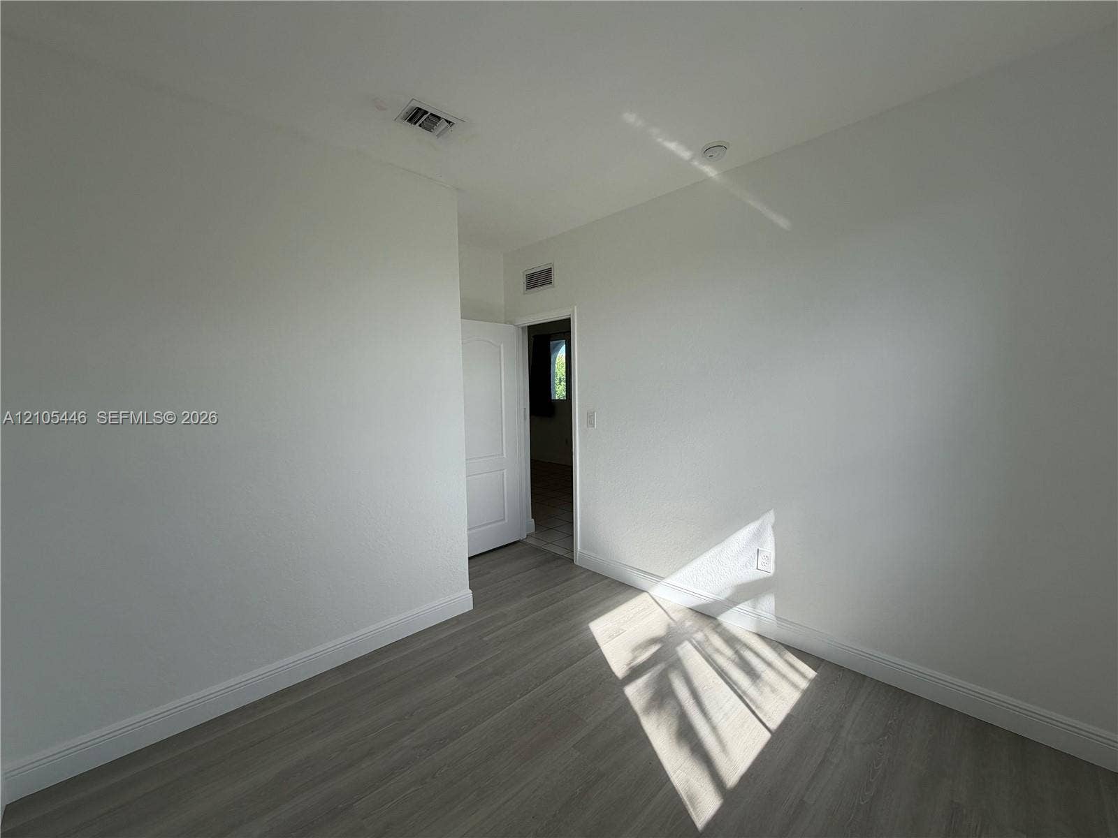Light-toned wood-finish flooring, white painted walls, and a white interior door