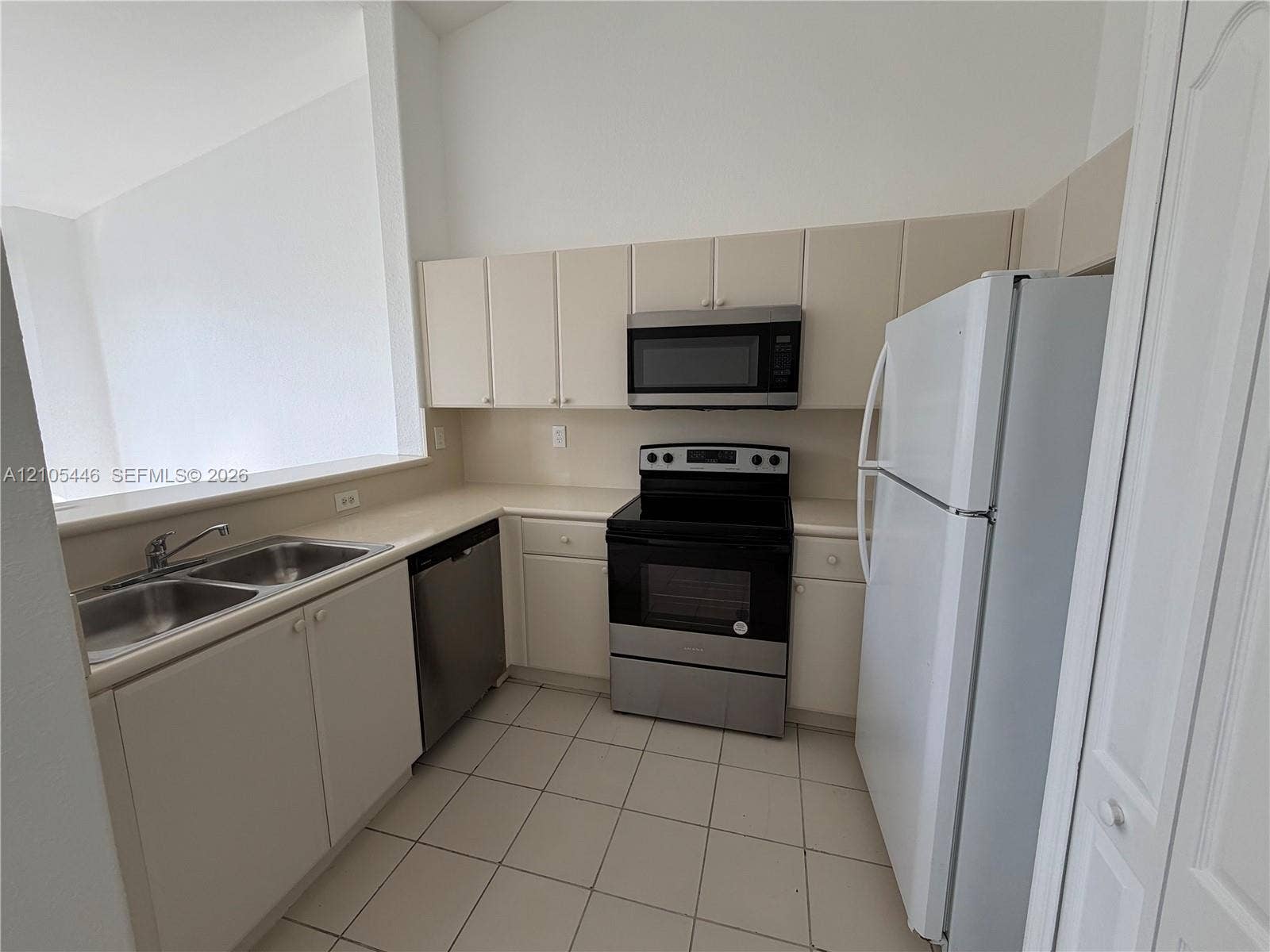 Kitchen featuring white cabinetry, light-toned countertops, a stainless steel microwave, a stainless steel and black range, and white tiled flooring