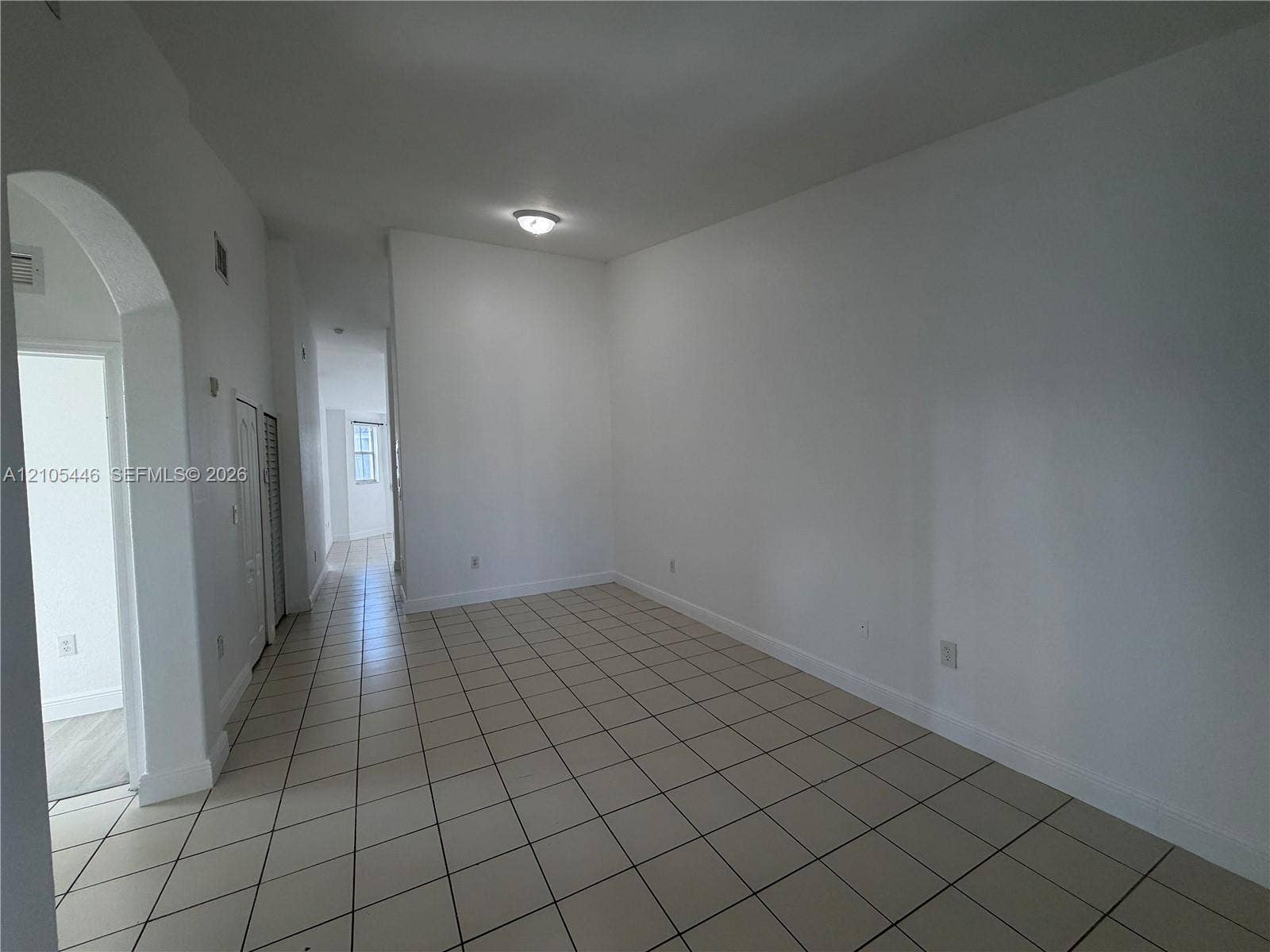 Spacious room featuring tile flooring, neutral wall tones, arched entryway, and flush-mount ceiling lighting