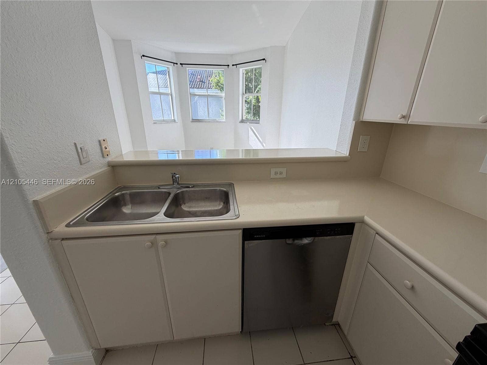 Double stainless steel sink, solid surface countertops, built-in dishwasher, white cabinetry, and bay windows