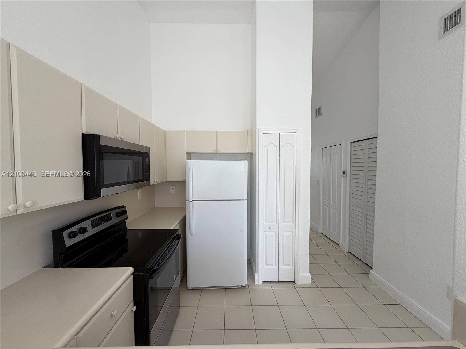 Kitchen featuring light-toned cabinetry, stainless steel microwave, black electric range, and light-toned countertops