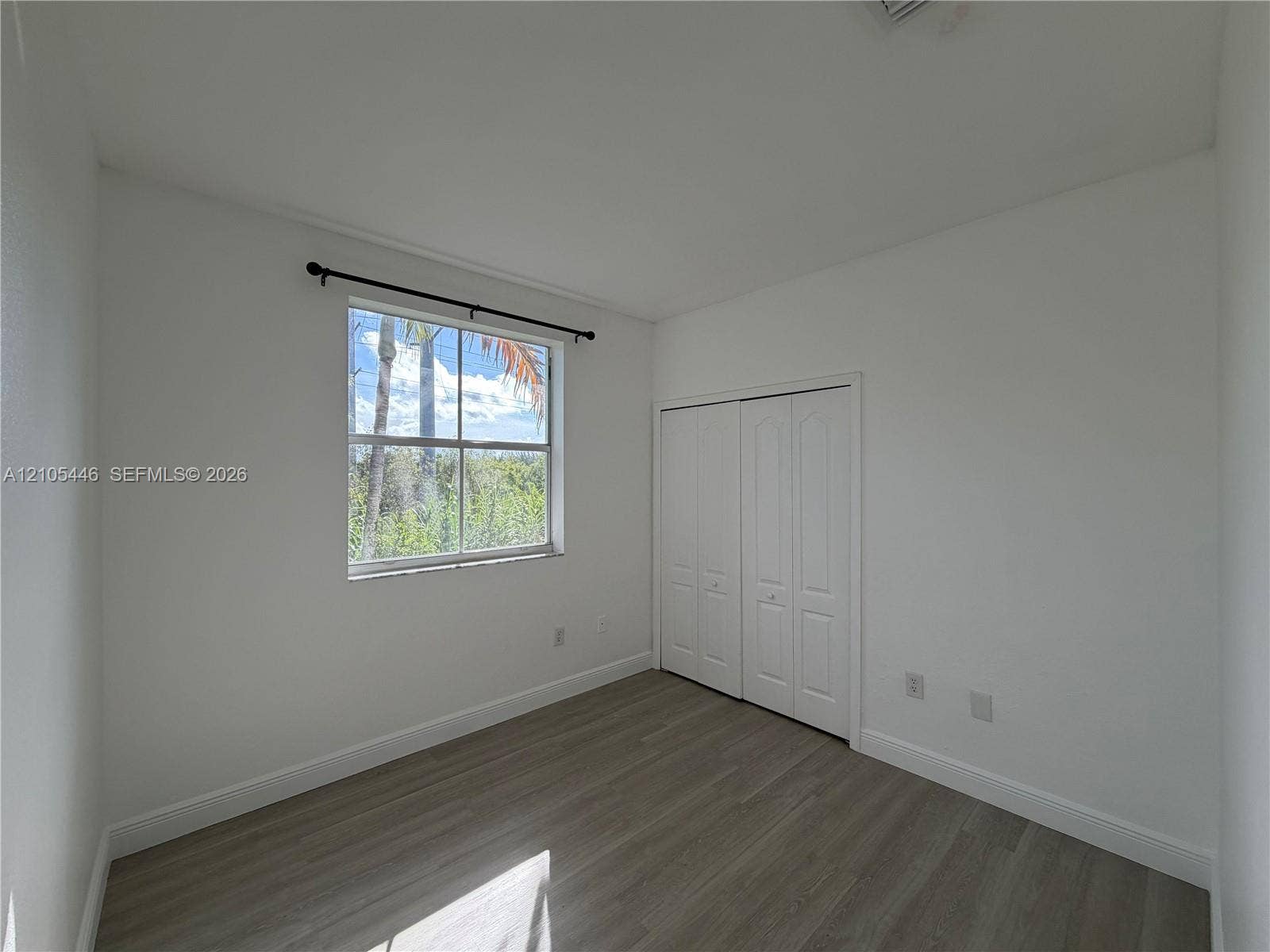 Light-toned wood-finish flooring, white walls, and a window with a black curtain rod